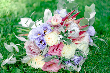 a bouquet of white roses and pink and violet eustomas with green leaves, a photo on a sunny day against a background of lush green grass