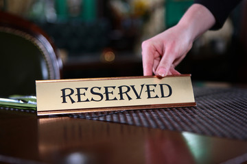 The waitress's hand puts a sign on the table that says reserve.Photo without faces, only hands.