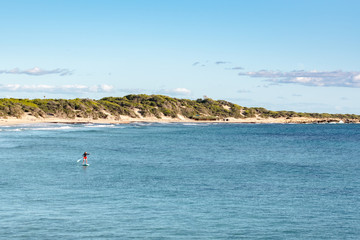 Man practicing paddle surfing through the deserted beaches of Ses Salines in the Ses Salinas National Park of Ibiza and Formentera, Spain.