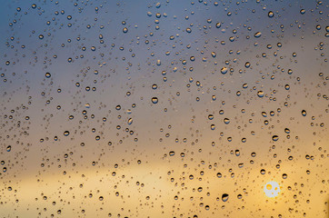 Rain outside window on background of sunset. Rain drops on glass during rain. Sunset outside window during raining. Bright texture of water drops