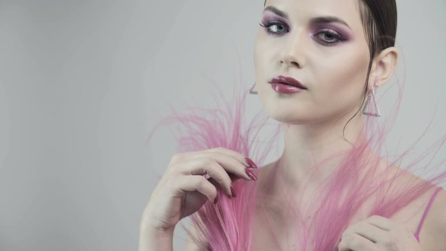 Glamorous young girl with pink make-up on her face with pink lip gloss. Luxurious pink feathers near the girl's face. Advertising perfume. Young woman hiding face with a pink feather.