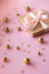 Gift in craft paper with a pink bow on a pink background with holographic sparkles in the form of stars and gold balls. Template  banner for greeting card your text design 2020. New year, christmas