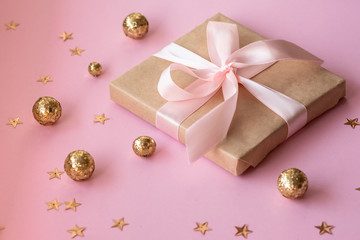 Gift in craft paper with a pink bow on a pink background with holographic sparkles in the form of stars and gold balls. Template  banner for greeting card your text design 2020. New year, christmas