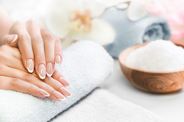 Obraz na płótnie Canvas Luxury nails french manicure concept. Woman in cosmetics salon with towels, salt in olive bowl and flowers in background. Relaxing hands massage or spa treatment procedure.