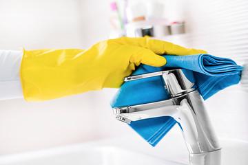 Woman maid or charwoman hand cleaning new modern bathroom, water tap clean detail, using yellow gloves and blue cloth.