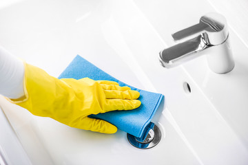 Woman maid or charwoman cleaning modern new basin in bathroom, water tap clean using yellow gloves and blue cloth.