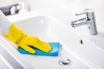 Woman maid or charwoman cleaning modern new basin in bathroom, water tap clean using yellow gloves...