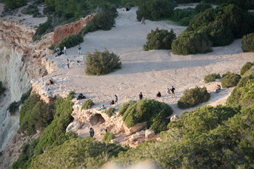 People at the Es Vedra viewpoint with sun falling behind Es Vedra with the Torre del Savinar in Es...