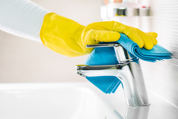 Woman maid hand cleaning new modern bathroom, water tap clean detail, using yellow gloves and blue cloth.