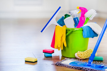 Basket or bucket with cleaning items on blurry modern kitchen background. Washing set colorful with...