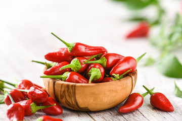 Red hot chili peppers in wooden bowl side view. Hot spicy pepper detail on white rustic table.
