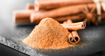 Cinnamon sticks spices on dark stone table. Cinnamons milled powder in white bowl on black board.