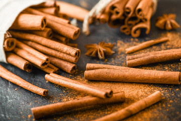 Cinnamon concept on stone table. Cinnamons sticks, powder and spices anise star on dark black board.