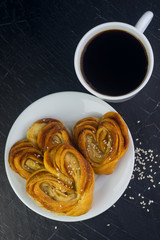  a white cup with coffee and a white plate with fresh homemade cakes on a black wooden tabletop with sprinkled sesame seeds Flat lay