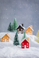 Miniature wooden houses village on the snow over blurred Christmas decoration background, toned