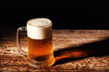 Beer. Cold Craft light Beer in a glass with water drops on the wooden table over the black background.
