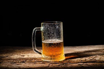 Beer. Cold Craft light Beer in a glass with water drops on the wooden table over the black background.