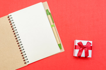 Open Notepad with pen and gift on red background. Flat position, top view. The concept of the holiday, Valentine's day, Christmas, New year
