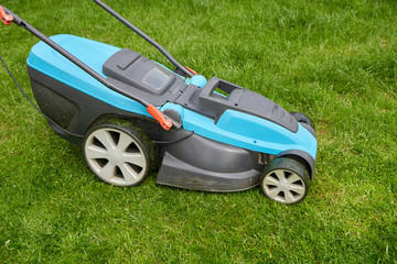 Electric lawn mower mows a bright green overgrown lawn, close-up