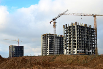 Tower cranes constructing a new residential building at a construction site against blue sky. Renovation program, development, concept of the buildings industry.