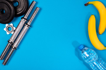 Fitness or bodybuilding. Sports equipment on a blue background, banana, water bottle, barbell, dumbbell, top view with plenty of copy space
