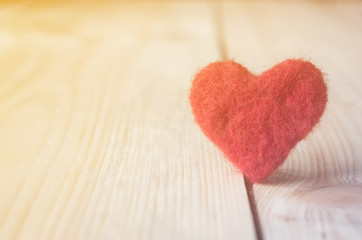 red heart made of wool on wooden background, a symbol of love, bright sun background