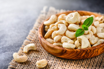 Cashew nuts in a wooden bowl on dark stone board with blurred background.