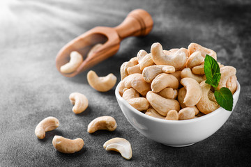 Cashew nuts in white porcelain bowl on dark stone table. Delicacies nut on black background.