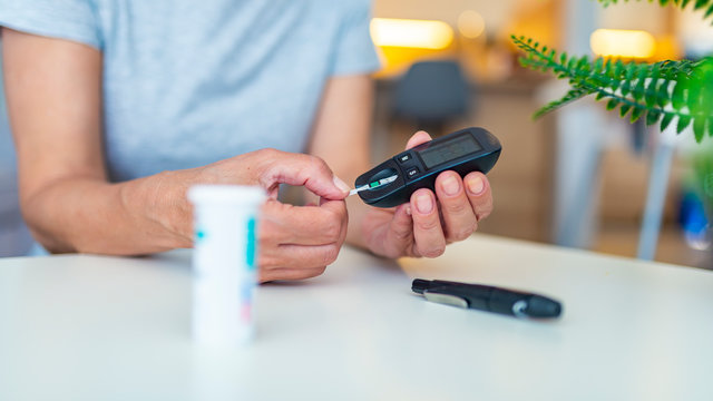 Woman checking blood sugar level while sitting at home. Woman using lancelet on finger. Diabetes checking blood sugar level. Woman using lancelet and glucometer at home.