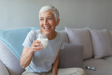 Senior woman's hands holding a glass of milk. Happy senior woman having fun while drinking milk at...