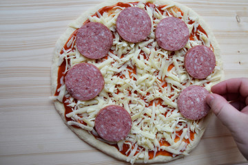 Raw, greased with tomato sauce pizza dough. The surface is strewn with mozzarella cheese. The chef puts sliced sausage. The process of cooking a delicious dish.