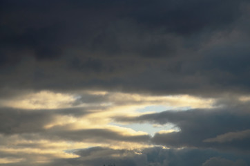 Evening sky. Dark clouds almost obscured the sunlight. You can see the gaps of the blue sky. Sunlight illuminates the clouds. A thunderstorm or heavy rain is coming.