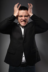 Angry business man in suit holding the head the hands on grey background. Closeup