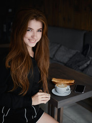 Cute redhead woman woman with adorable smile sitting in cozy city cafe enjoying free time coffee break with cappuccino and dessert dressed black blouse and shorts