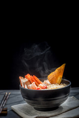 Noodles with steam and smoke in bowl on wooden background, selective focus. Asian meal on a table, junk food concept