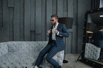 Handsome stylish man in blue suit in a cage at home siting on sofa near mirror