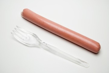 Sausage and a transparent fork on a white background. The concept of fast food, hunger or lack of food, cheap GMO products for one. Environmental issue, poor student or senior citizen.