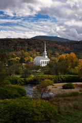 Fototapeta na wymiar Spot of sun on Stowe Community Church on a cloudy day with Fall colors at Stowe Vermont
