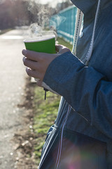Young man with steaming cup of coffee in the park. Coffee to go concept.