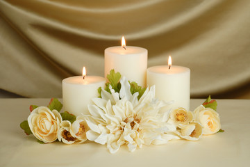 Fototapeta na wymiar Elegant white candles with cream and white roses and white dahlia flower with a gold satin background. Home interior floral table arrangement. Wedding card