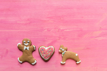 Festive, decorated gingerbread man cookies on pink wooden background. Christmas greeting cards concept with space for text