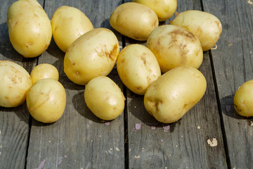 Lots of young and fresh potatoes on a black wooden table.