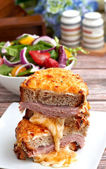 Sandwich with Parmesan and Gruyere cheese, ham, béchamel sauce and artisan bread accompanied by a salad on a wooden background.  The Croque Monsieur.