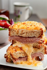 Sandwich with Parmesan and Gruyere cheese, ham, béchamel sauce and artisan bread accompanied by a salad on a wooden background.  The Croque Monsieur.