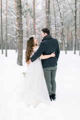 Back view of couple in love are hugging on background of the snowy forest. Winter wedding.