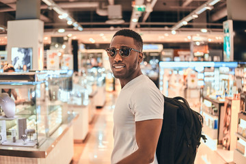 Happy smiling man with backpack feels good in between nice showcases at the shop.