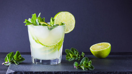 Cocktail mojito and mint on black background. Refreshing cocktail with lime and fresh mint on slate board. Summer drink with citrus and ice. Widescreen