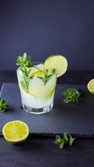 Cocktail mojito and mint on black background. Refreshing cocktail with lime and fresh mint on slate board. Summer drink with citrus and ice. Widescreen