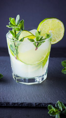 Cocktail mojito and mint on black background. Refreshing cocktail with lime and fresh mint on slate board. Summer drink with citrus and ice. Widescreen
