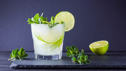 Cocktail mojito and mint on black background. Refreshing cocktail with lime and fresh mint on slate board. Summer drink with citrus and ice. Widescreen